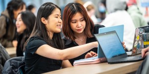 Two women are pointing at the laptop. 
