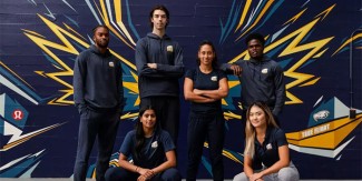 A group of athletic-looking students pose in navy blue UBC-branded athletic gear, in front of a navy blue brick wall.